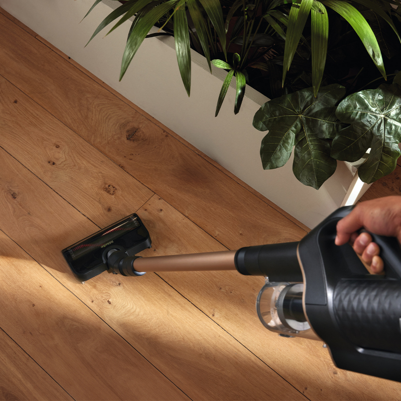 Akku-Staubsauger Miele Duoflex saugt Staub auf hellem Holzfußboden unter Zimmerpflanzen