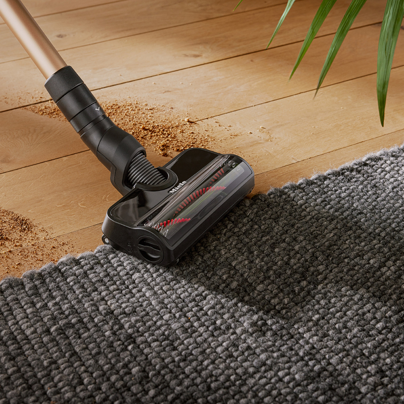Miele Duoflex Elektrobürste saugt Schmutz von Teppichkante auf Holzboden