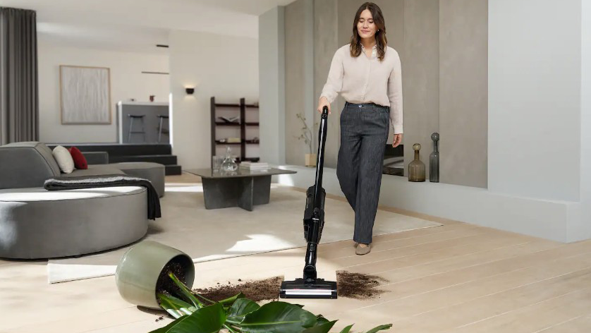 Eine Frau saugt Erde und Pflanzenreste mit einem Miele Akku-Staubsauger im Wohnzimmer auf.