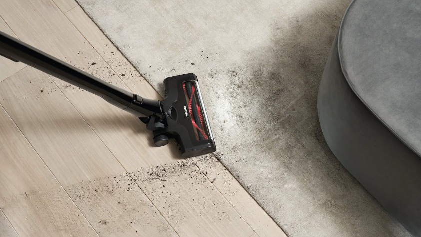 Ein Miele Akku-Staubsauger entfernt Staub entlang eines Teppichrandes